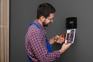 Technician installing home security alarm system on gray wall indoors