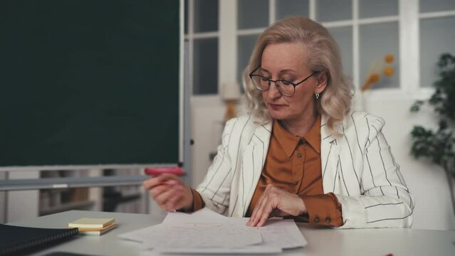 Overworked middle-aged teacher grading students homework, feeling stressed