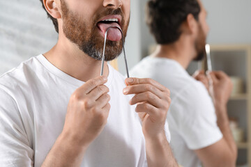 Man brushing his tongue with cleaner in bathroom, closeup. Space for text - obrazy, fototapety, plakaty