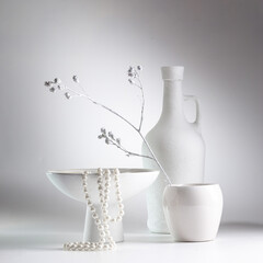 White still life with white dishes and a pearl necklace on a white background