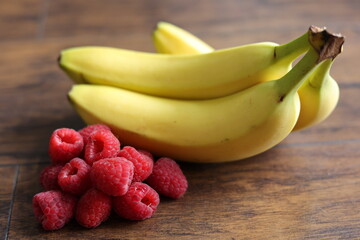 Bunch of bananas and handful of raspberries spread on laminated floor.