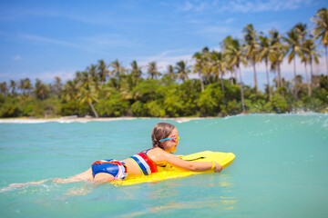 Child surfing on tropical beach. Surfer in ocean.