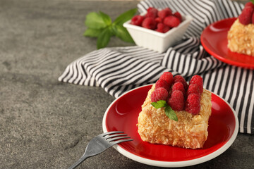 Piece of delicious Napoleon cake with fresh raspberries served on grey table, closeup. Space for text
