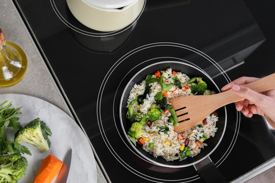 Woman frying rice with vegetables on induction stove, top view