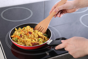 Woman frying rice with meat and vegetables on induction stove, closeup