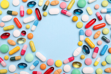 Frame made of many different pills on light blue background, flat lay. Space for text