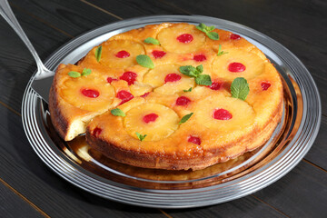Taking piece of delicious cut pineapple pie with cherry and mint on dark wooden table