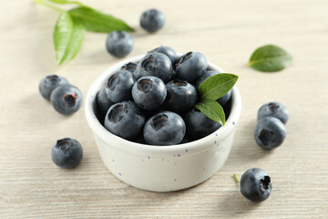 Bowl of fresh tasty blueberries on white wooden table, closeup
