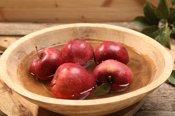 Fresh red apples in bowl with water on wooden table, closeup