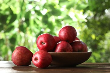 Ripe red apples and bowl on wooden table outdoors