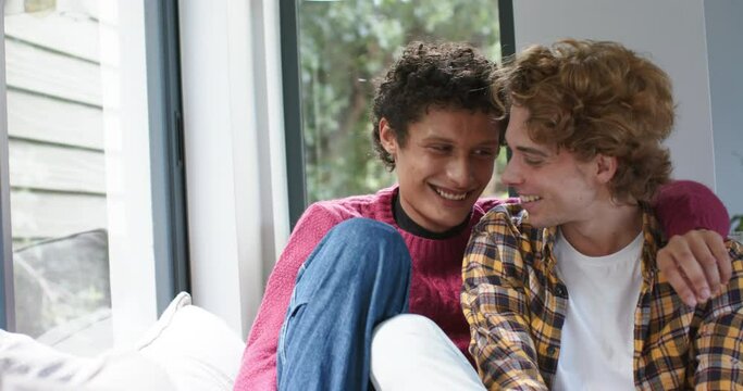 Portrait of happy diverse gay male couple embracing and smiling at home, slow motion