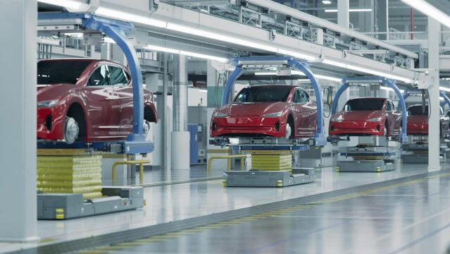 EV Production Line on Advanced Automated Bright Factory. High Performance Electric Car Manufacturing. Car Batteries being Attached to Electric Vehicles on Assembly line. AGV Transport Batteries.