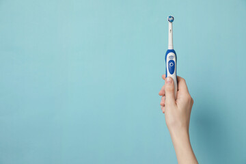 Woman holding electric toothbrush on light blue background, closeup. Space for text