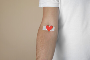 Blood donation concept. Man with adhesive plaster on arm against beige background, closeup. Space...