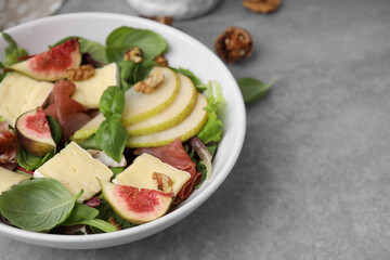 Tasty salad with brie cheese, prosciutto, pear and figs on grey table, closeup. Space for text