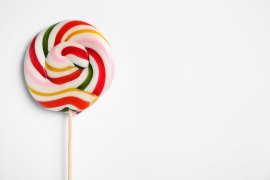 Stick with bright lollipop on white background, top view. Space for text