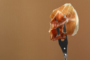 Fork with slice of tasty jamon on brown background, closeup. Space for text