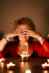 middle aged woman with red sweater, waiting for her birthday surprise, blowing out the candles on the cake, birthday cupcake