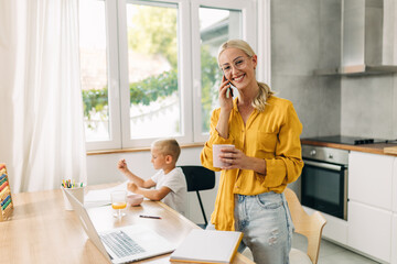 Single mom working form home while her son is sitting at the table and drawing.