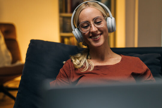 Closeup view of a young Caucasian woman with headphones looking at laptop screen.