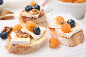 Tasty sandwiches with brie cheese, fresh berries and walnuts on white table, closeup