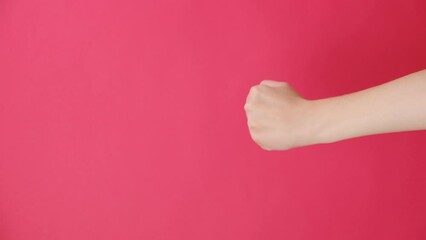 Vertical shot of angry unknown young woman shaking fist, isolated over red studio background wall with copy space. Advertising area, mock up. Threat gesture, concept of aggression, warning, punishment