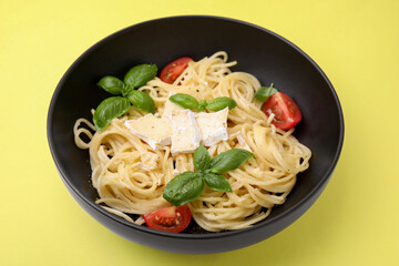 Bowl of delicious pasta with brie cheese, tomatoes and basil leaves on yellow background, closeup