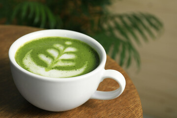 Delicious matcha latte in cup on wooden coffee table, closeup. Space for text