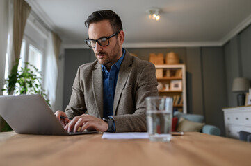 Low angle view of focused manager dressed in elegant suit working over laptop on desk at home