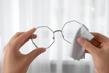 Woman wiping her glasses with microfiber cloth at home, closeup