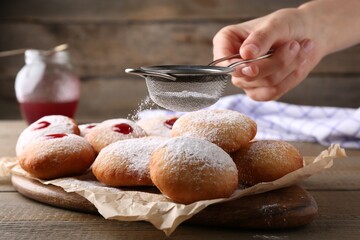Woman dusting powdered sugar onto delicious Hanukkah donuts on wooden table, closeup