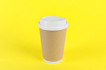 Paper cup with plastic lid on yellow background. Coffee to go