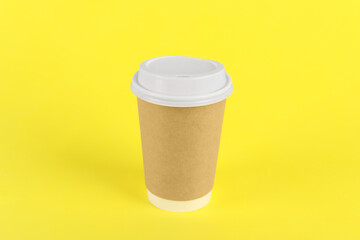 Paper cup with plastic lid on yellow background. Coffee to go