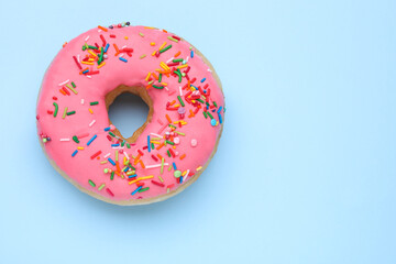 Glazed donut decorated with sprinkles on light blue background, top view. Space for text. Tasty confectionery