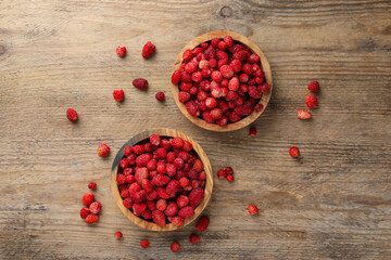 Fresh wild strawberries in bowls on wooden table, flat lay