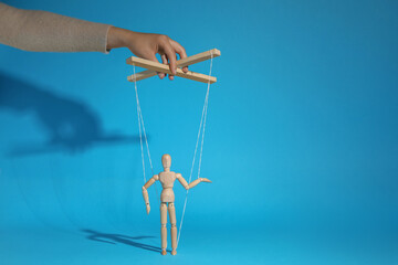 Woman pulling strings of puppet on light blue background, closeup