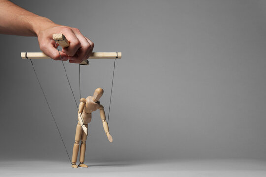 Man pulling strings of puppet on gray background, closeup. Space for text