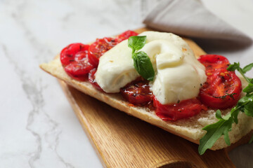 Toast with delicious burrata cheese, tomatoes and arugula on white marble table, closeup. Space for text