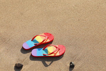 Fototapeta na wymiar Stylish rainbow flip flops on sand at beach, above view. Space for text