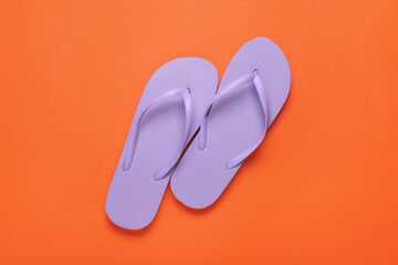 Stylish violet flip flops on orange background, top view