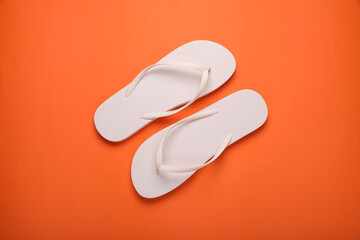 Stylish white flip flops on orange background, top view