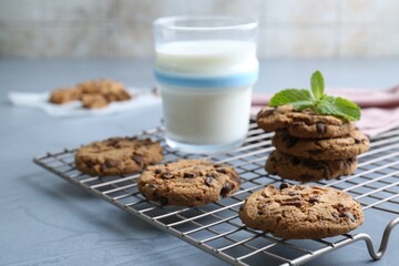 Tasty chocolate chip cookies, glass of milk and mint leaves on light grey table