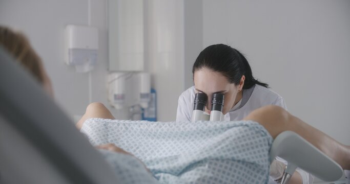 Gynecology room in modern clinic. Female gynecologist uses colposcope, takes tests from patient. Woman lies on gynecological chair during colposcopy procedure. Preparation for pregnancy. Slow motion.