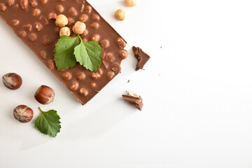 Chocolate bar with hazelnuts and leaves on white table