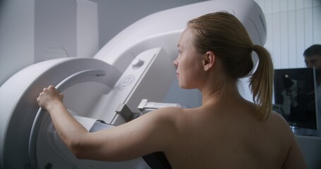 Adult woman stands topless undergoing mammography scanning checkup in clinic radiology room. Male...