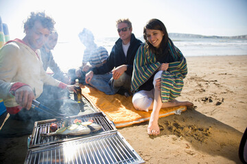 Friends sitting around a barbeque on the beach
