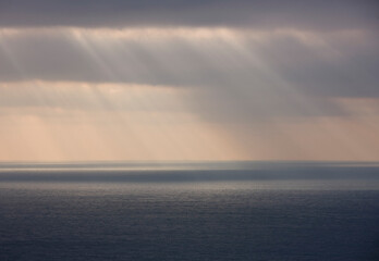 Grey sky with rain and sun rays shining on the ocean

