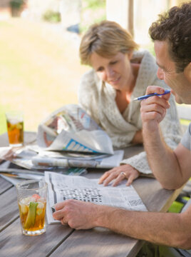 Couple sitting outside drinking cocktails and doing crossword
