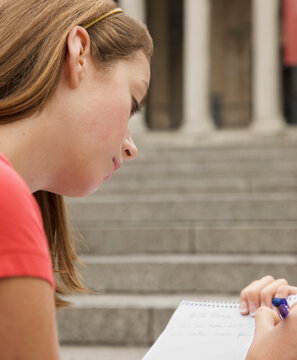 Teenaged girl taking notes opposite a city building
