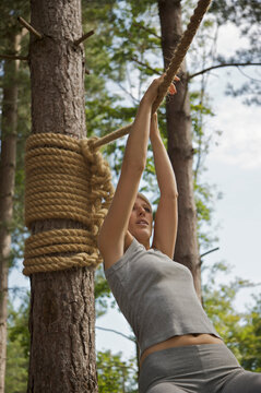 Young woman at obstacle course hanging from a rope
